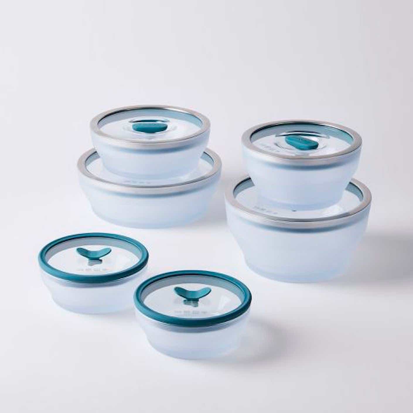 A set of six microwave-safe clear glass bowls with plastic and metal lids are stacked on top of each other.