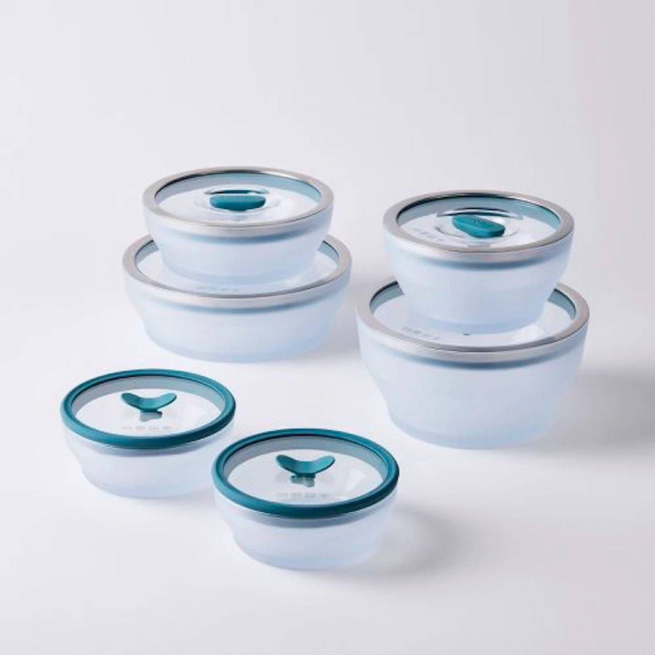 A set of six microwavable clear glass bowls with plastic and metal lids are stacked on top of one another.
