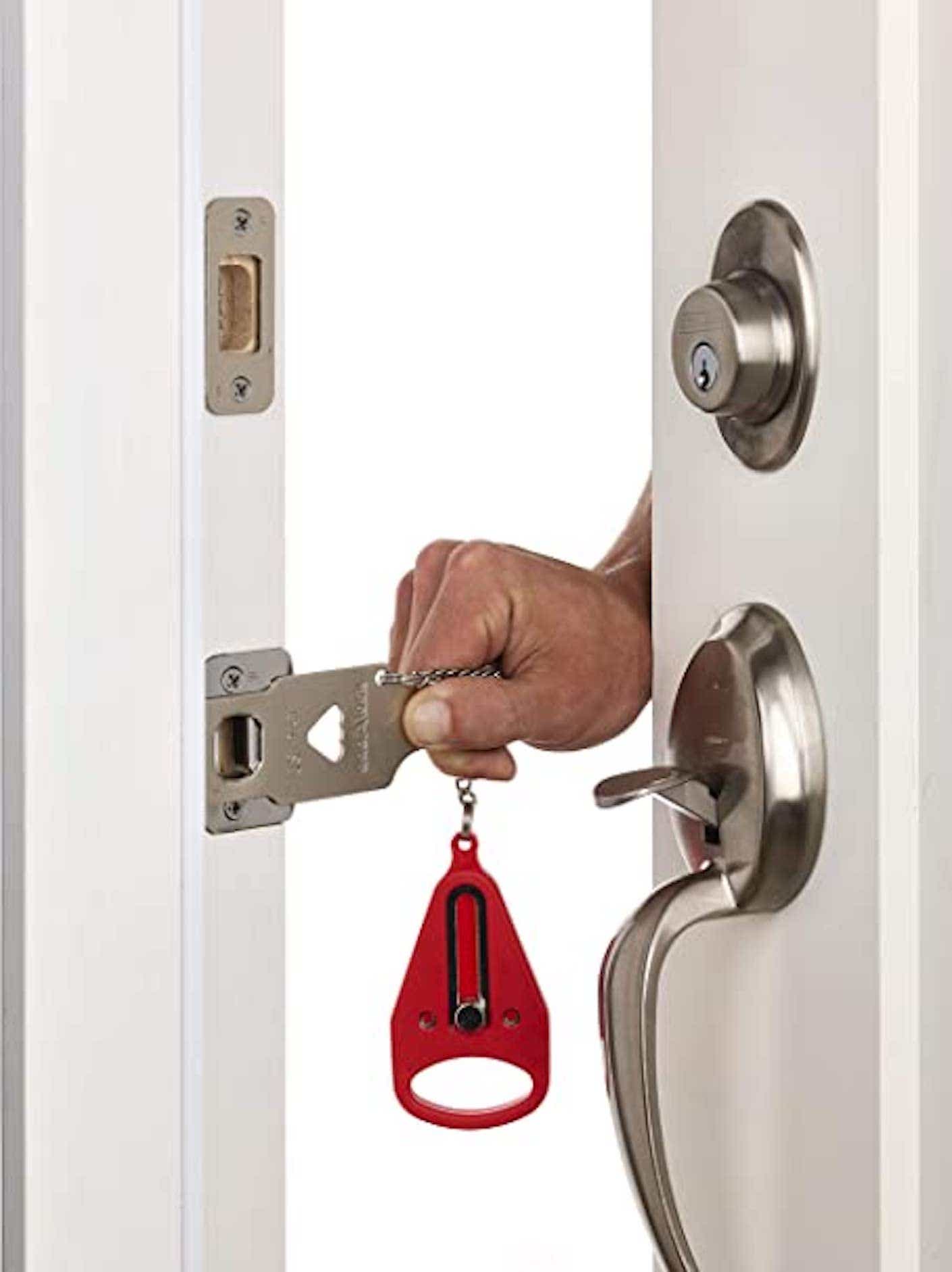 A hand inserts a simple, flat, metal door lock into the side of a door near the doorknob.