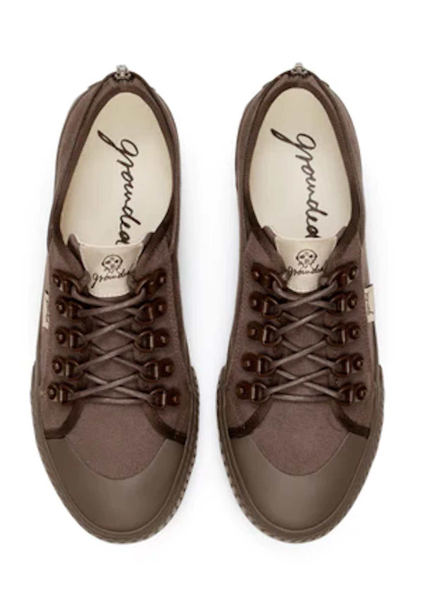 A pair of classic brown canvas sneakers with rubber tips and laces stand in front of a white background.