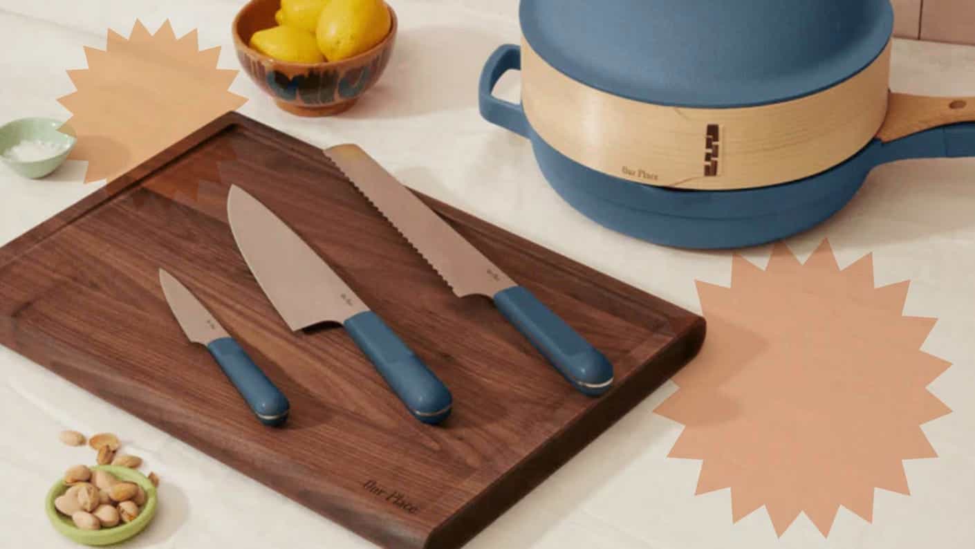 Three sharp knives (a serrated knife, a chef's knife, and a paring knife) with blue handles rest on a dark wood cutting board on a white counter.