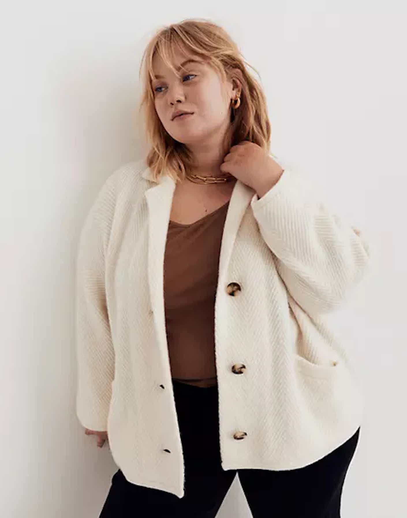 A woman wears a button down, off-white, thick cardigan sweater.