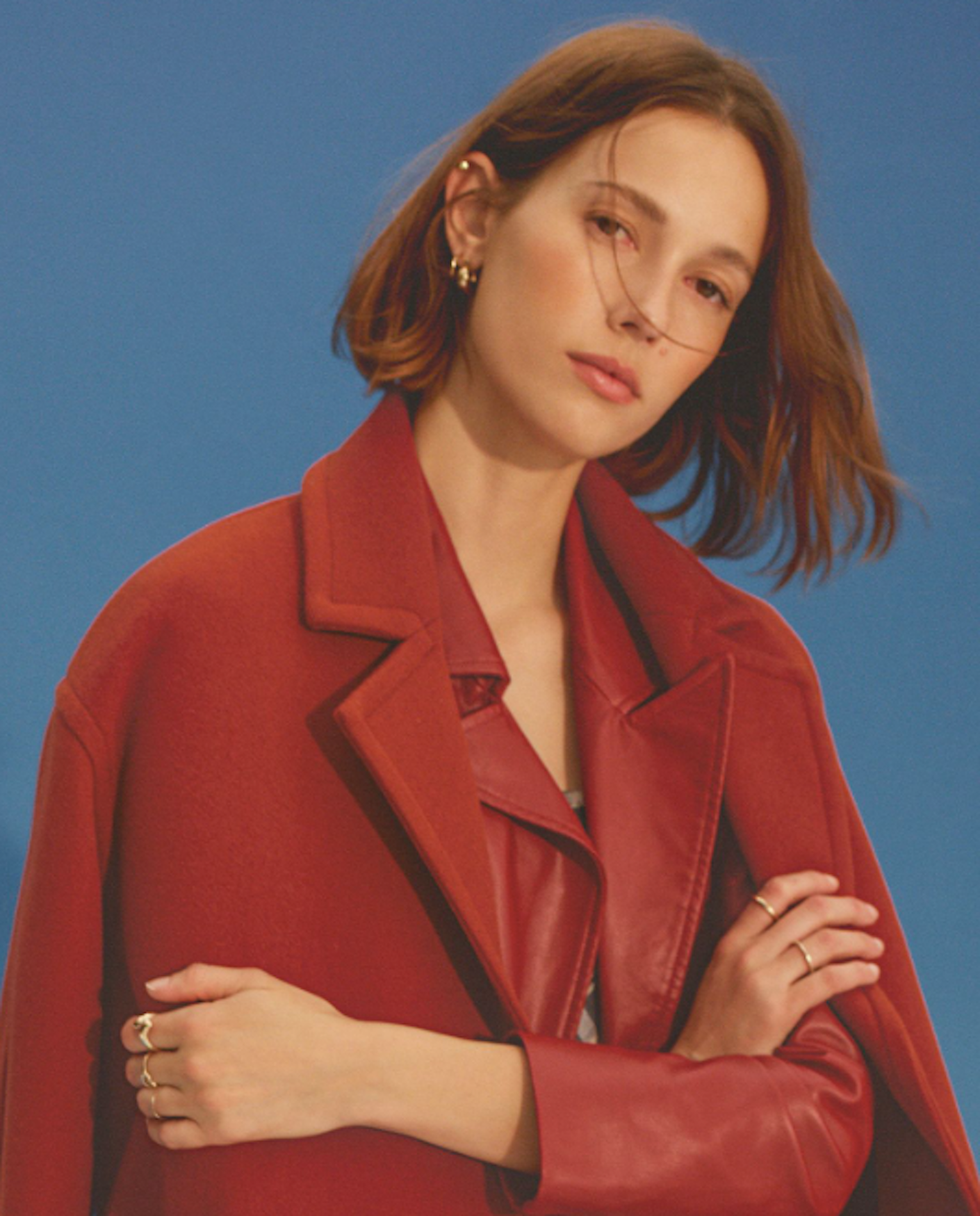 A woman wearing a red blazer crosses her arms and stares at the camera.