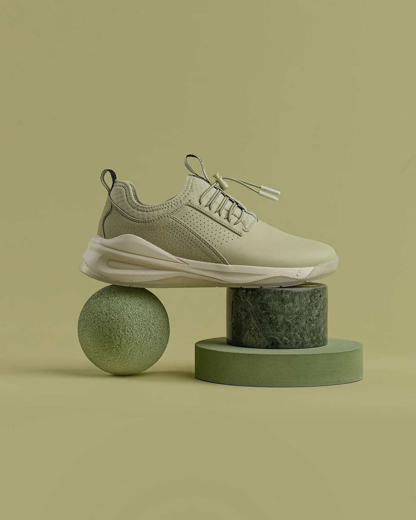 A sage green mesh sneaker with a lighter green sole balanced on a lime and two green blocks.