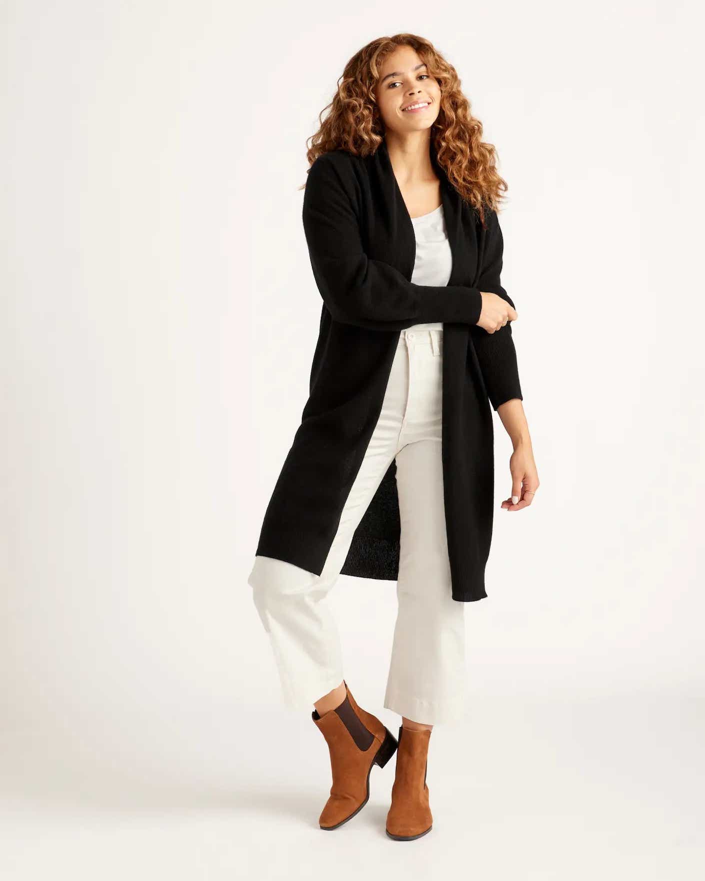 A knee-length black sweater duster is pictured on a relaxed looking woman.