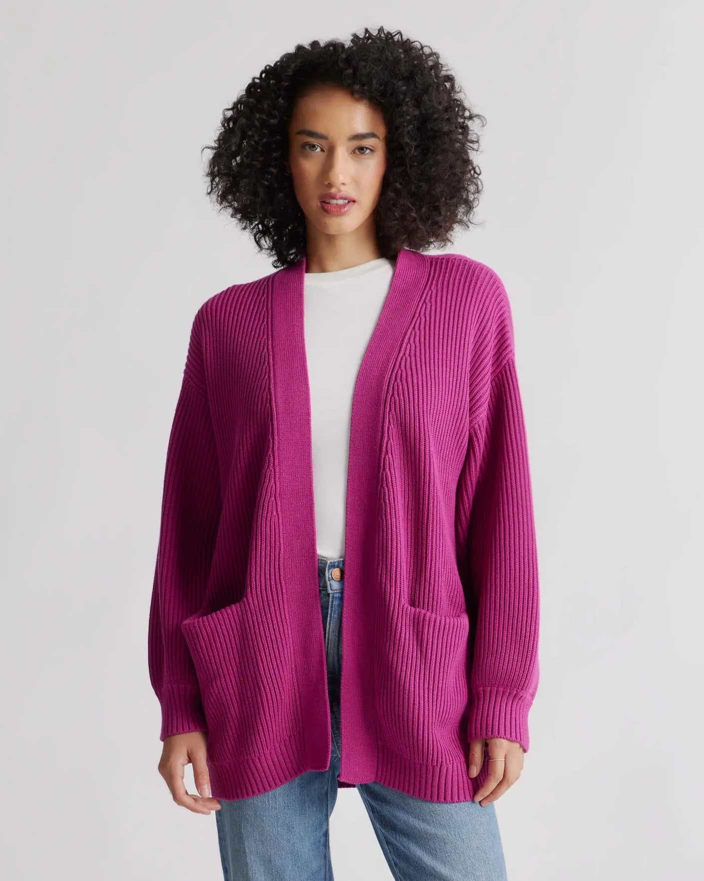 A woman wears an open front cardigan that is bright fuschia, soft, and falls below the hip.