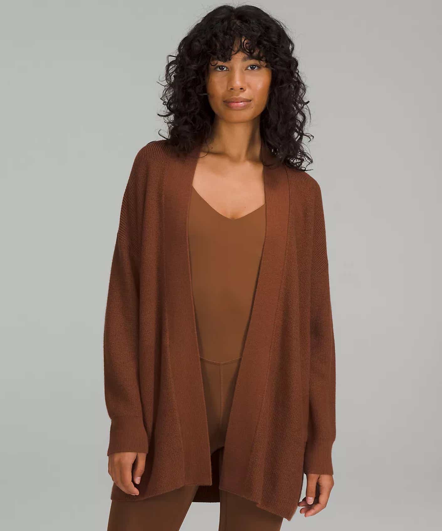 A woman wears a brown top and brown leggings underneath a brown cardigan sweater with a draped open front.