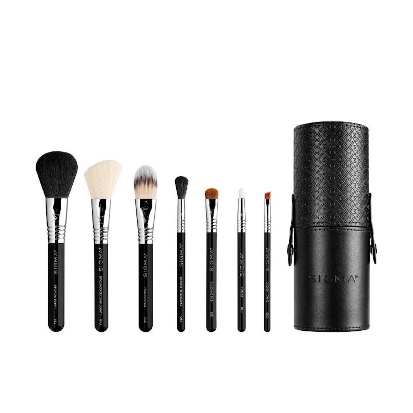 Seven brushes of different types are lined up next to a portable cylindrical brush holder.