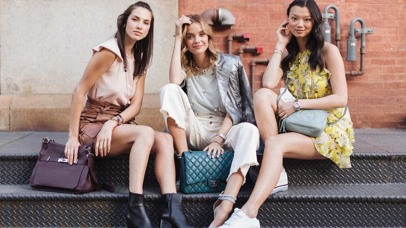 A trio of women sitting on steps wear luxurious handbags and jewelry.