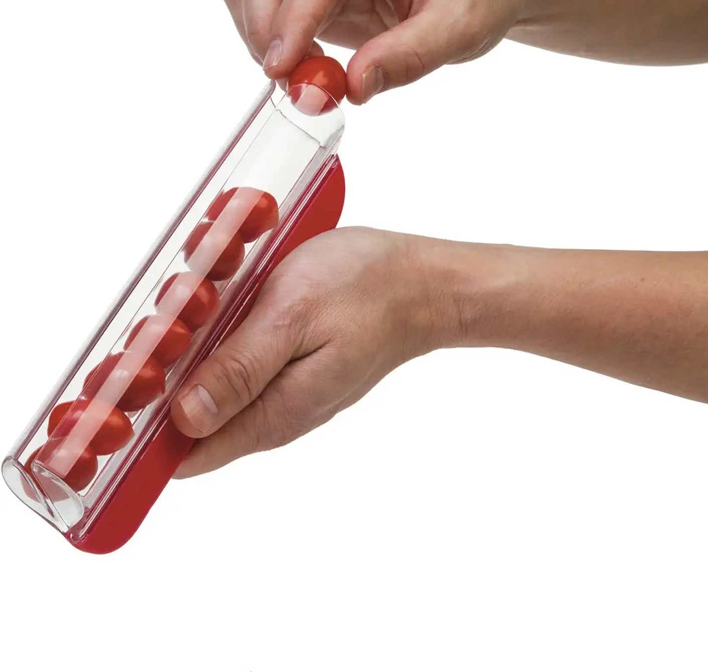 A hand places a row of cherry tomatoes into a zip slicer that can cut through all the tomatoes at once.