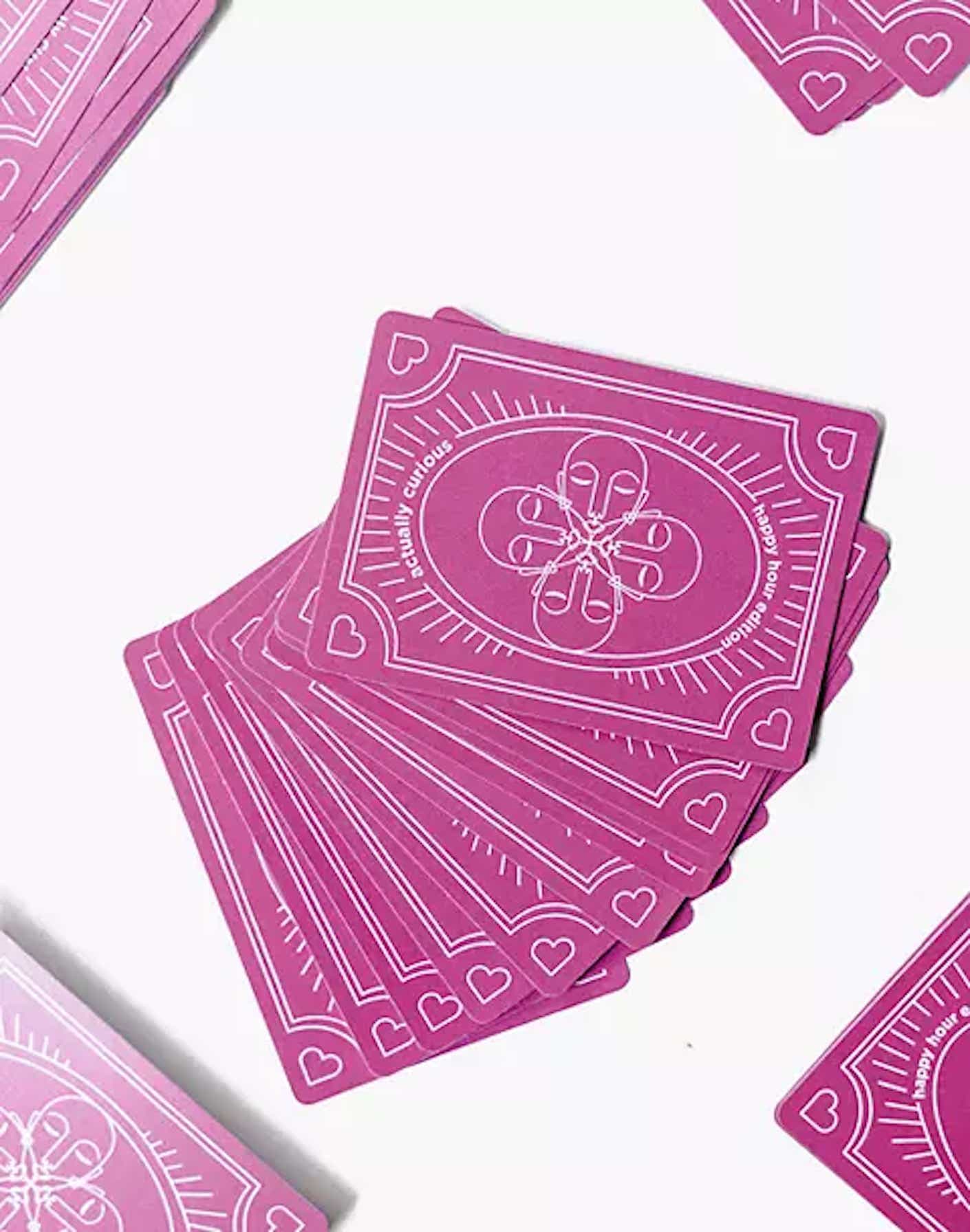 A deck of pink cards with white patterned details are spread out onto a white table.