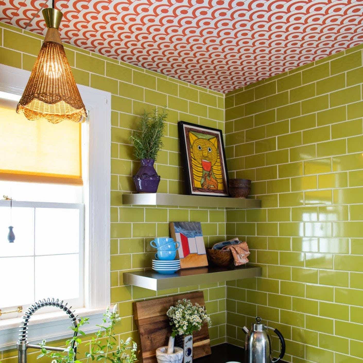 A kitchen features pea green tile peel and stick wallpaper that contrasts the red and white penny tile papered ceiling.