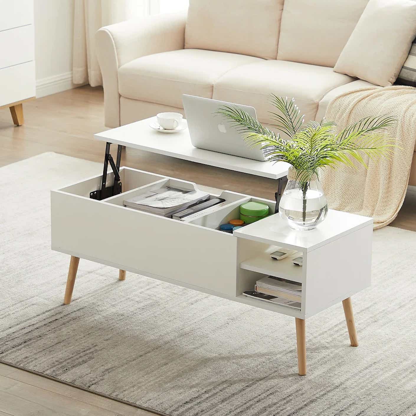 A white storage coffee table with light wooden legs sits open to show off inner compartments and shelves.