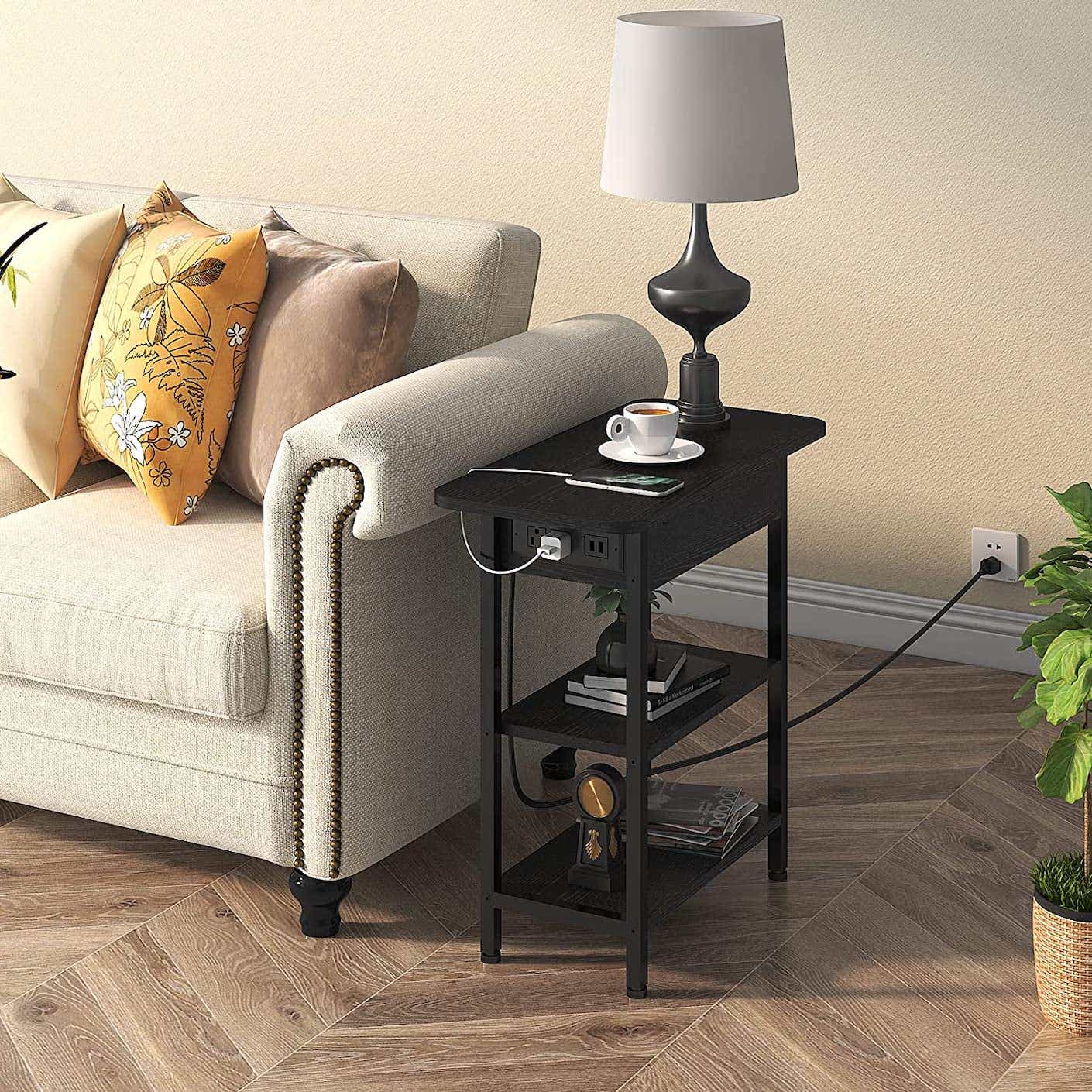 A black end table with charging ports sits next to a plush sofa.