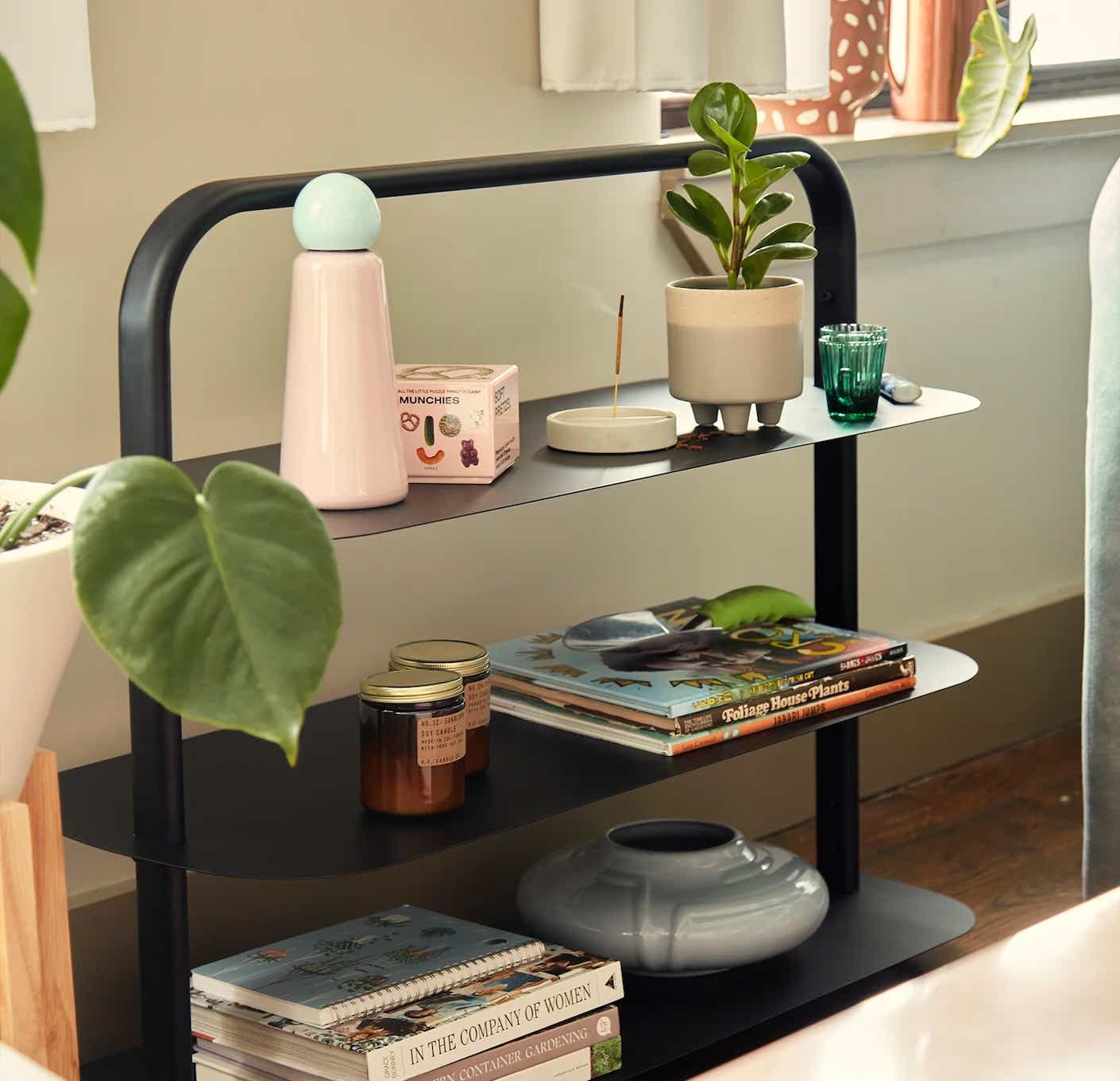 A black metal entryway rack is decorated with houseplants, books, and candles.