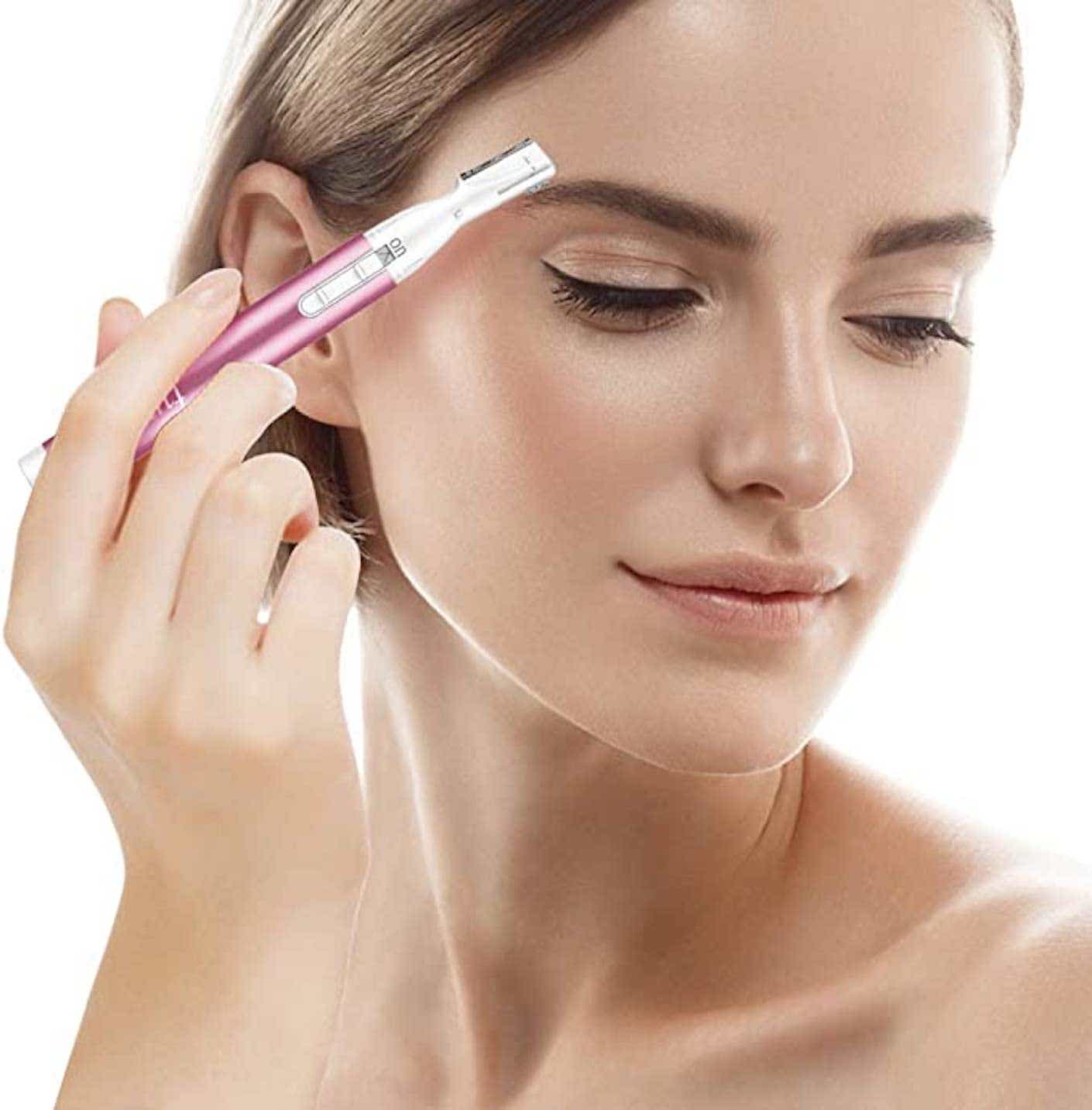 A woman holds an electric eyebrow trimmer up to her face.