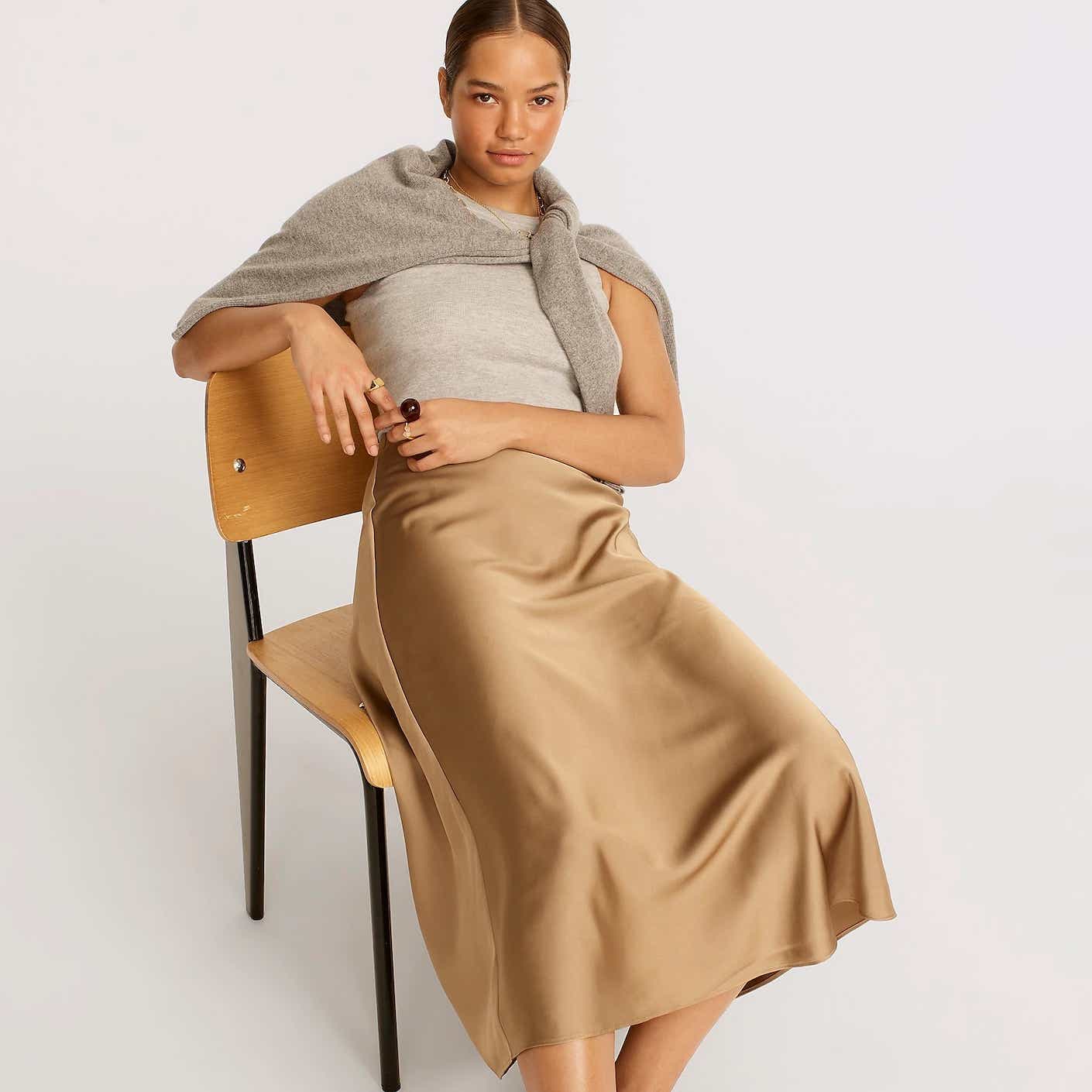 A woman lounges in a tan silk maxi skirt that is cut like a slip.