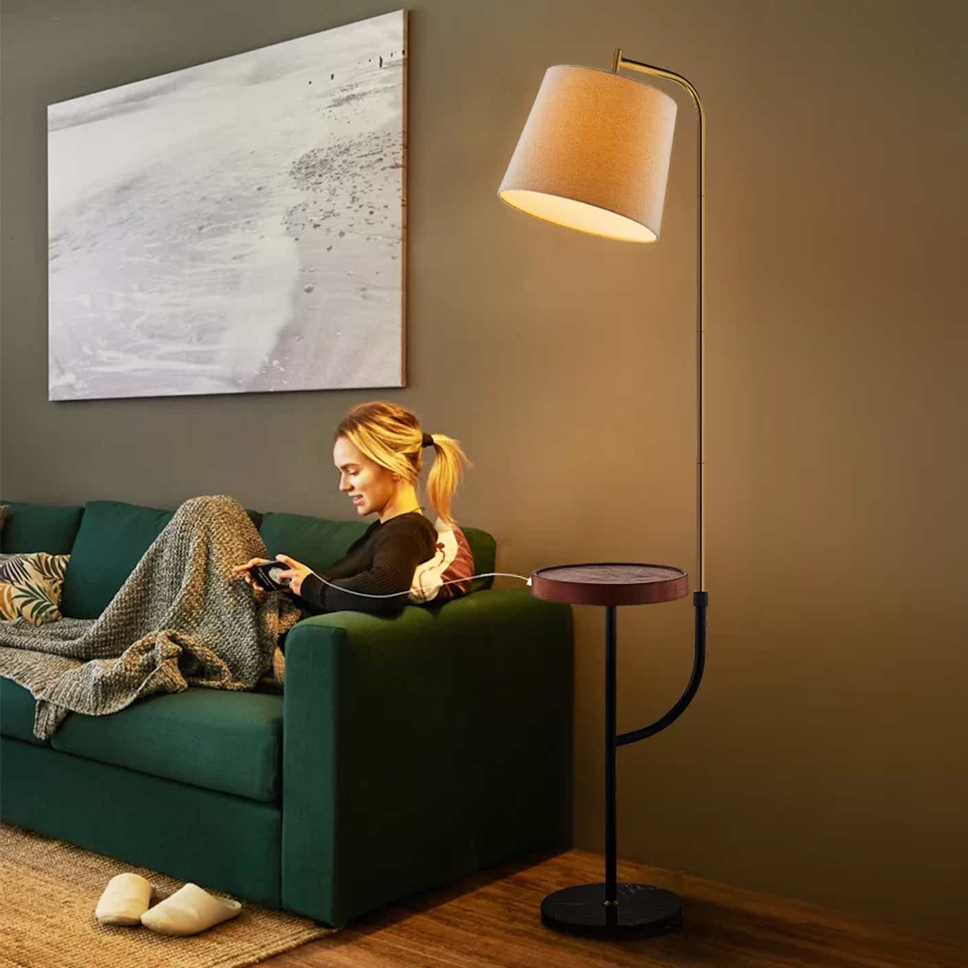 A floor lamp with attached circular tray is shown warmly illuminating a living room space.