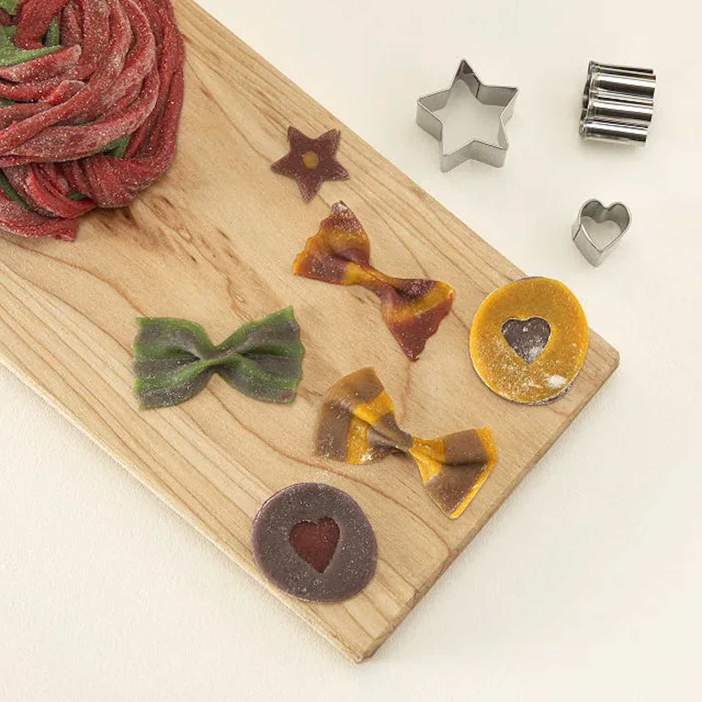 A wooden cutting board is adorned with colorful, multi colored bowtie pasta.