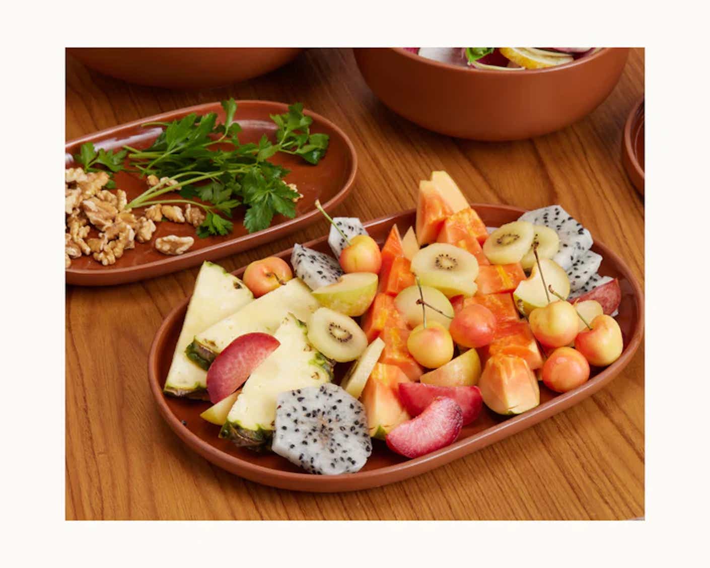A flat serving platter with rounded edges holds an array of colorful fruits.