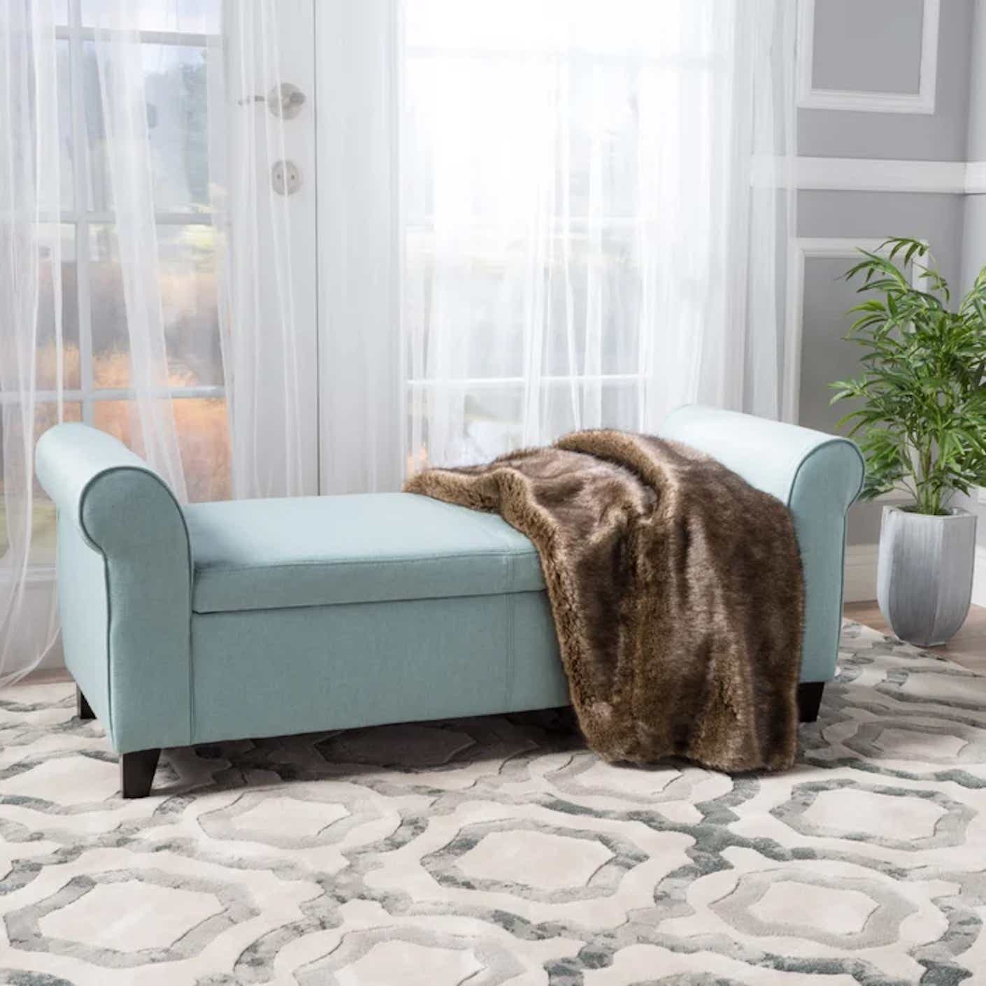 A long, rectangular, baby blue ottoman is pictured looking like a chaise lounge; however, it contains storage space inside.