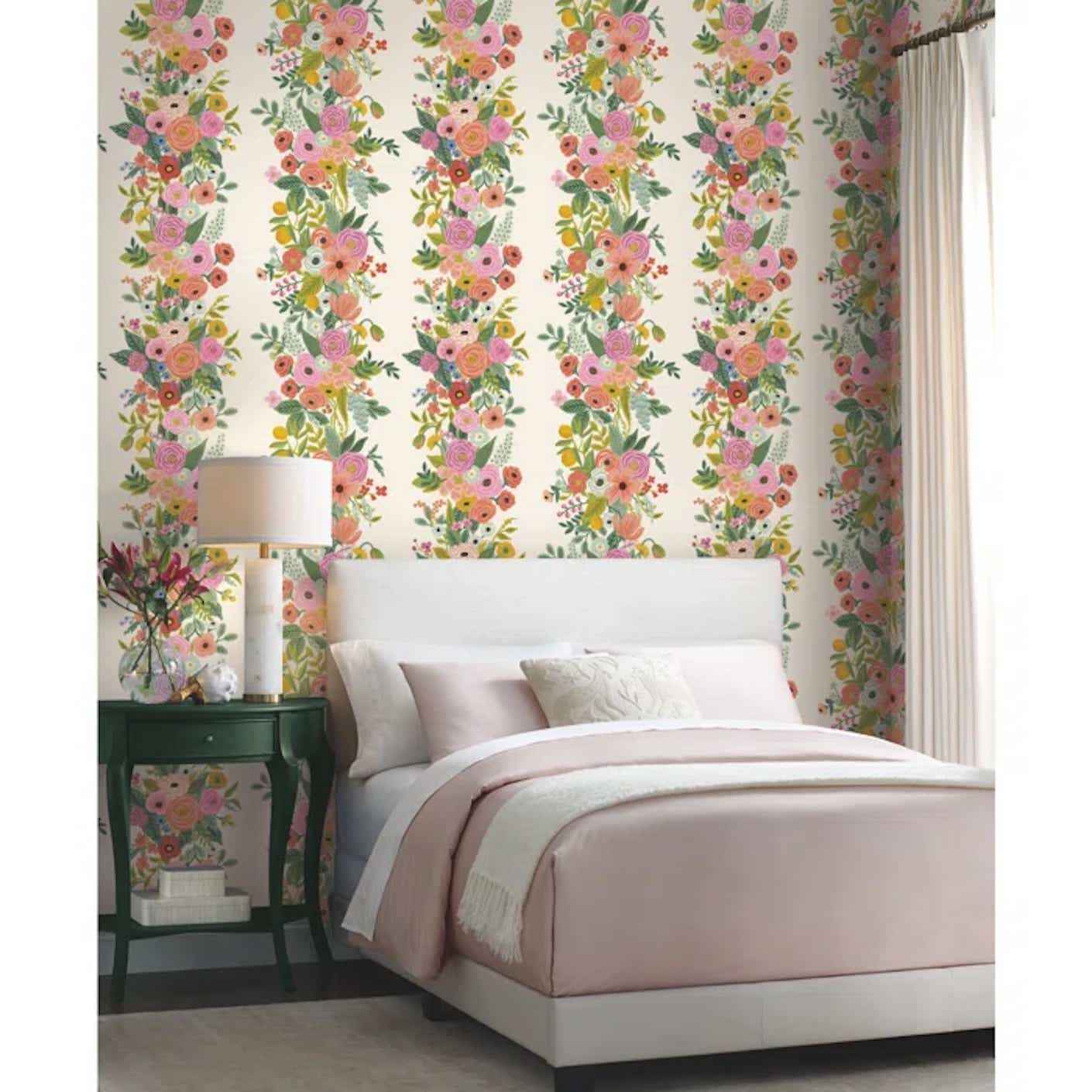 A white and light pink bed sits in front of light pink and green floral wallpapered wall.