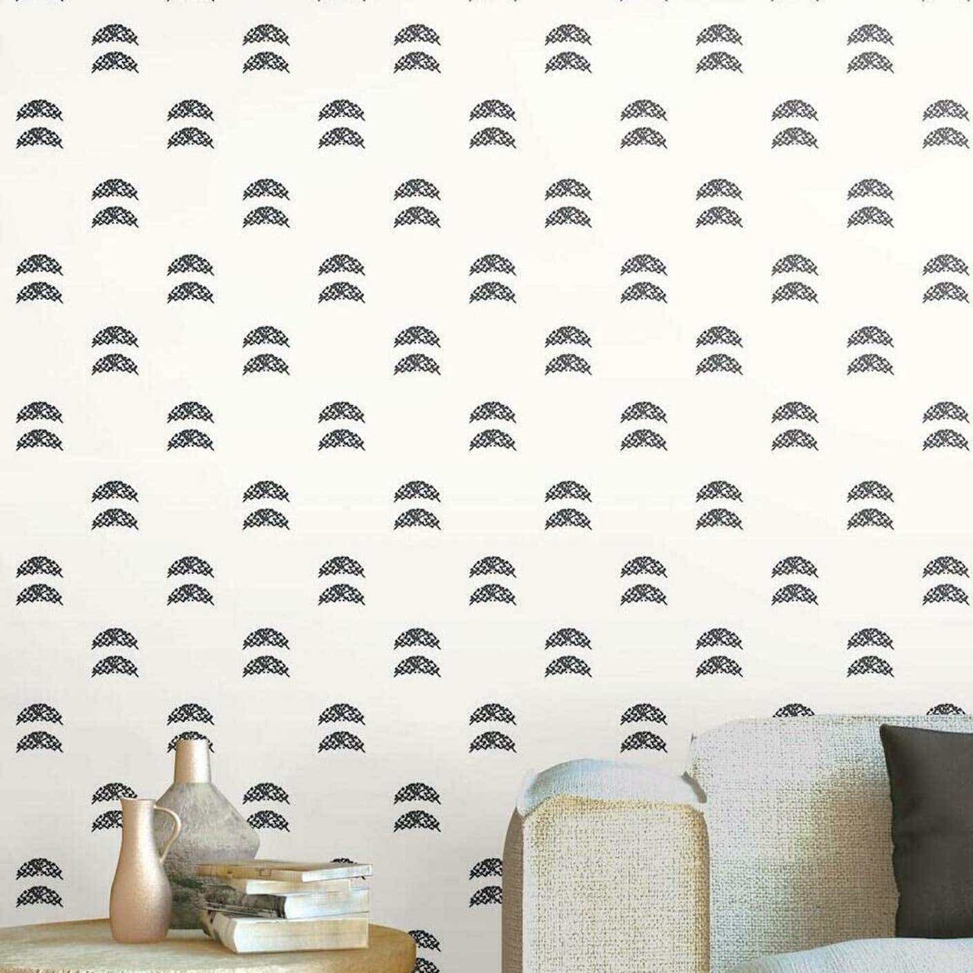 A grey couch and end table stand in front of a wall covered in white wallpaper with black half moon print.