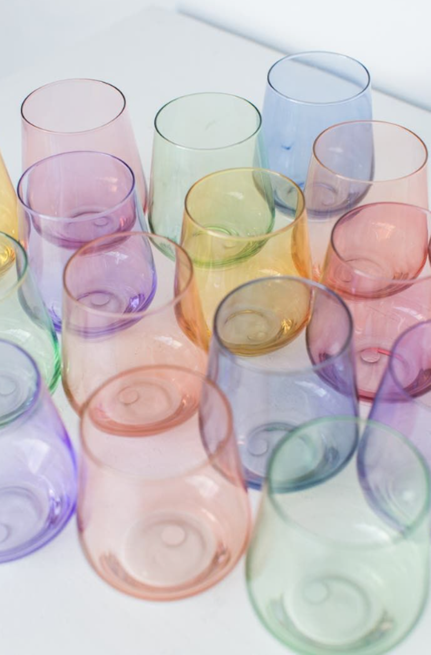 A table full of clear, colored, stemless wine glasses sit on a white table.