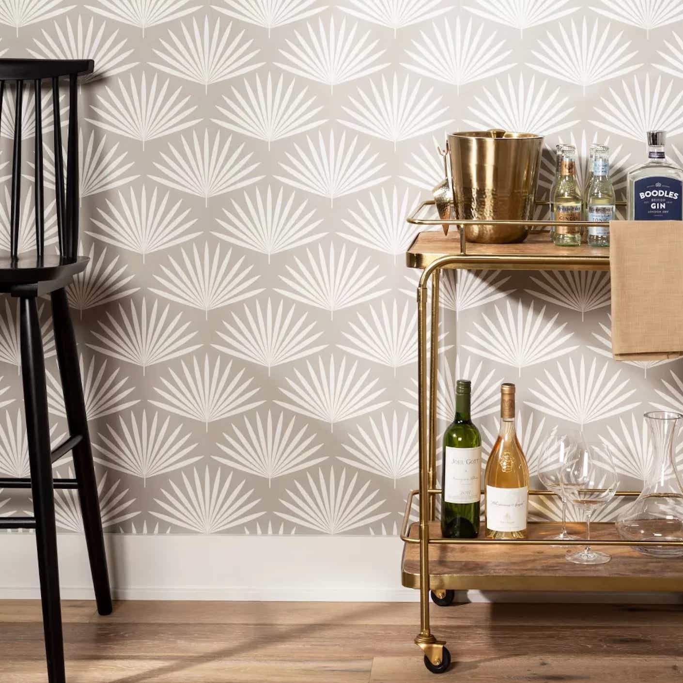 A chair and bar cart stand in front of a wall covered in grey wallpaper with white palm front pattern.