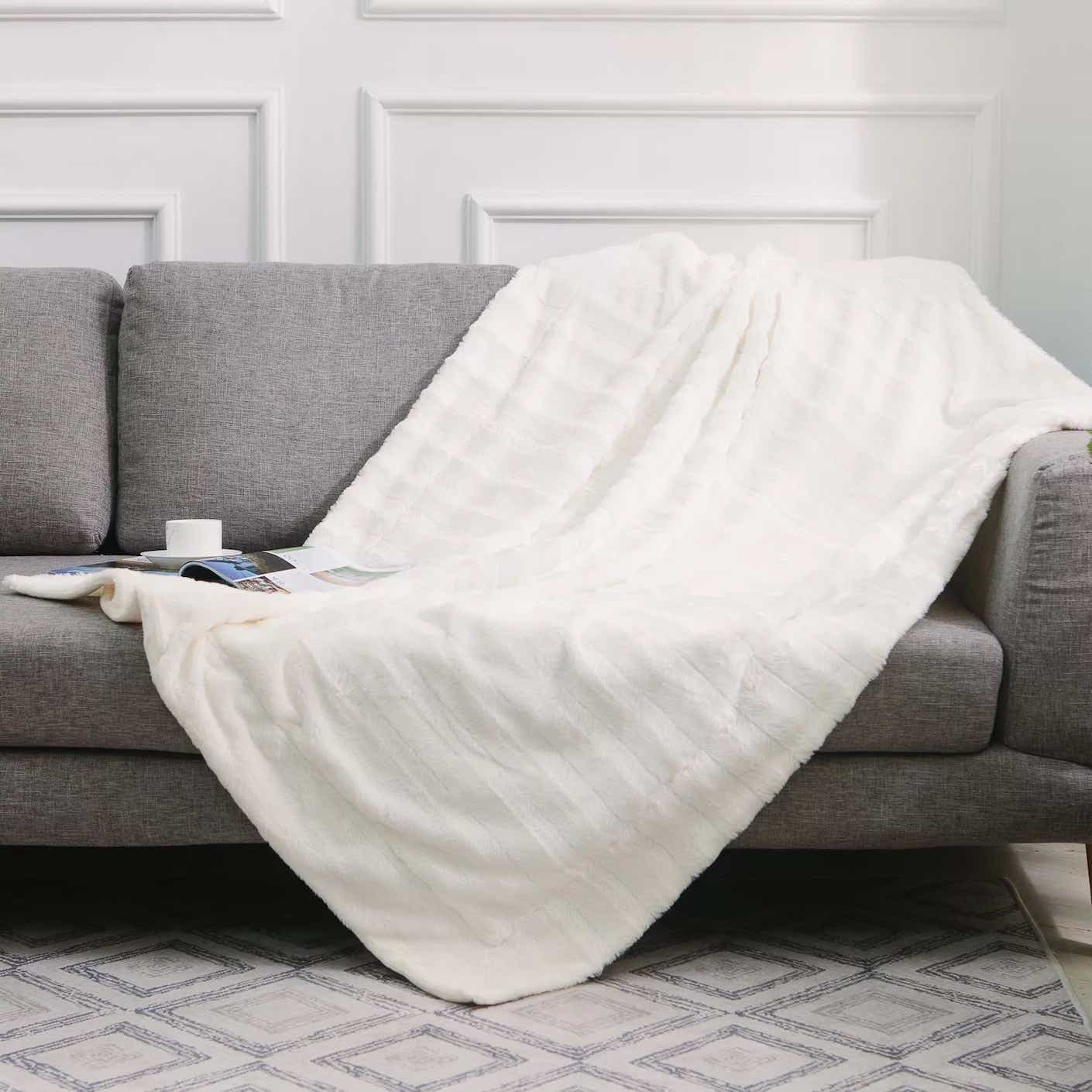 A soft, white, throw blanket is tossed across a grey couch.