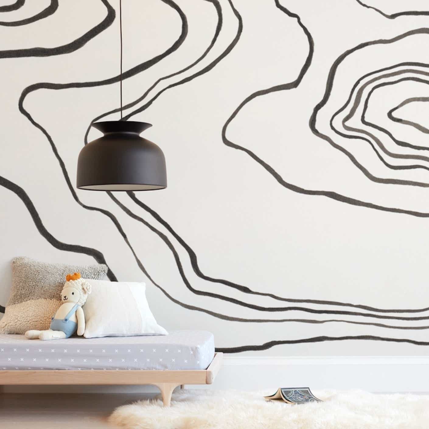 A low futon sits in front of a wall papered with off-white wallpaper that has a large, painterly, abstract, inky black pattern of ripples undulating outwards.