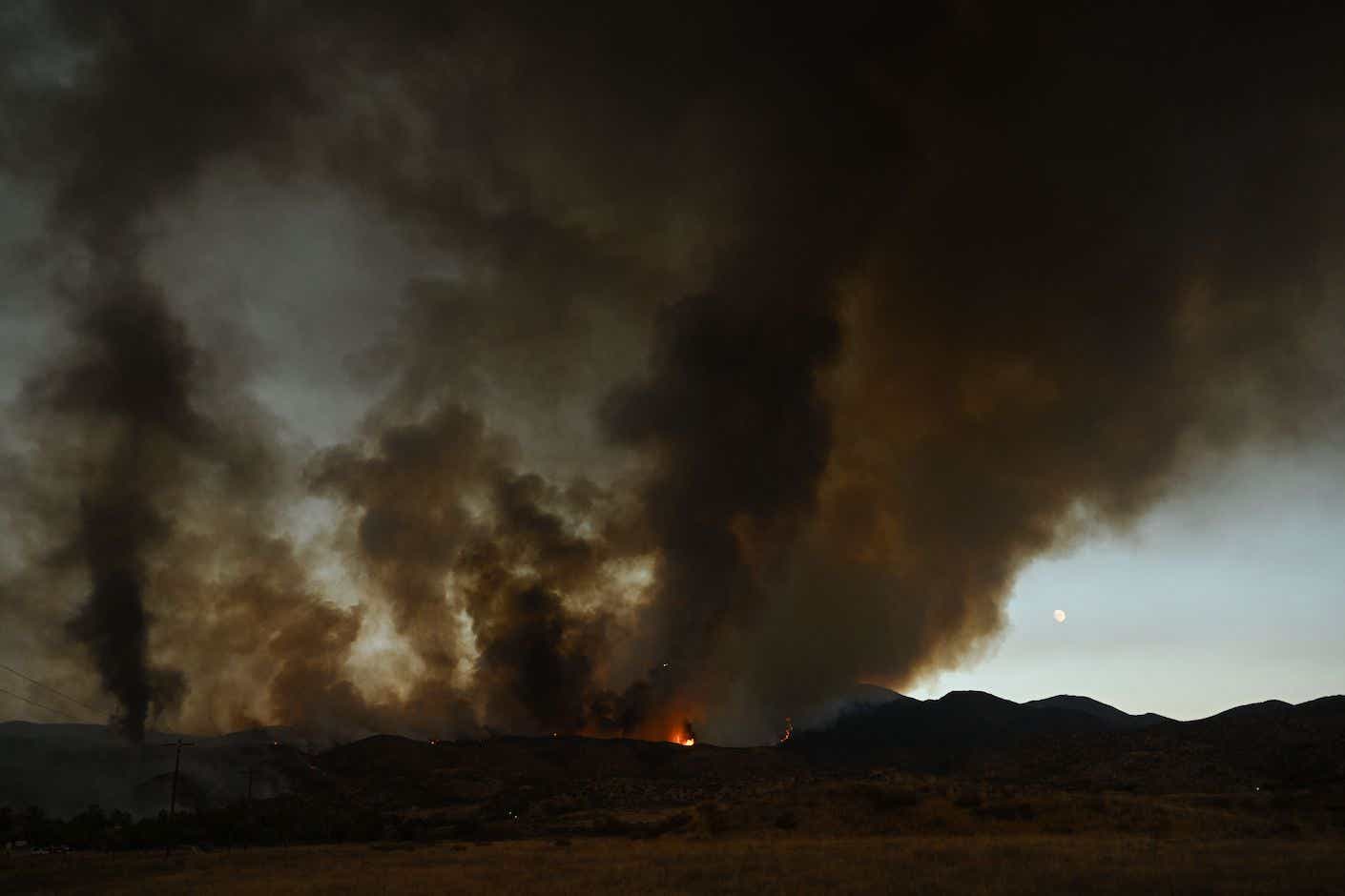 The moon rises (R) as plumes of smoke from a wildfire flow into the air during the Fairview Fire near Hemet, California in Riverside County on September 7, 2022. - A ferocious heat wave scorching the western United States could finally begin to wane in the coming days, forecasters said on September 7, but they warned of dangerous fire conditions as howling winds sweep through the bone-dry region