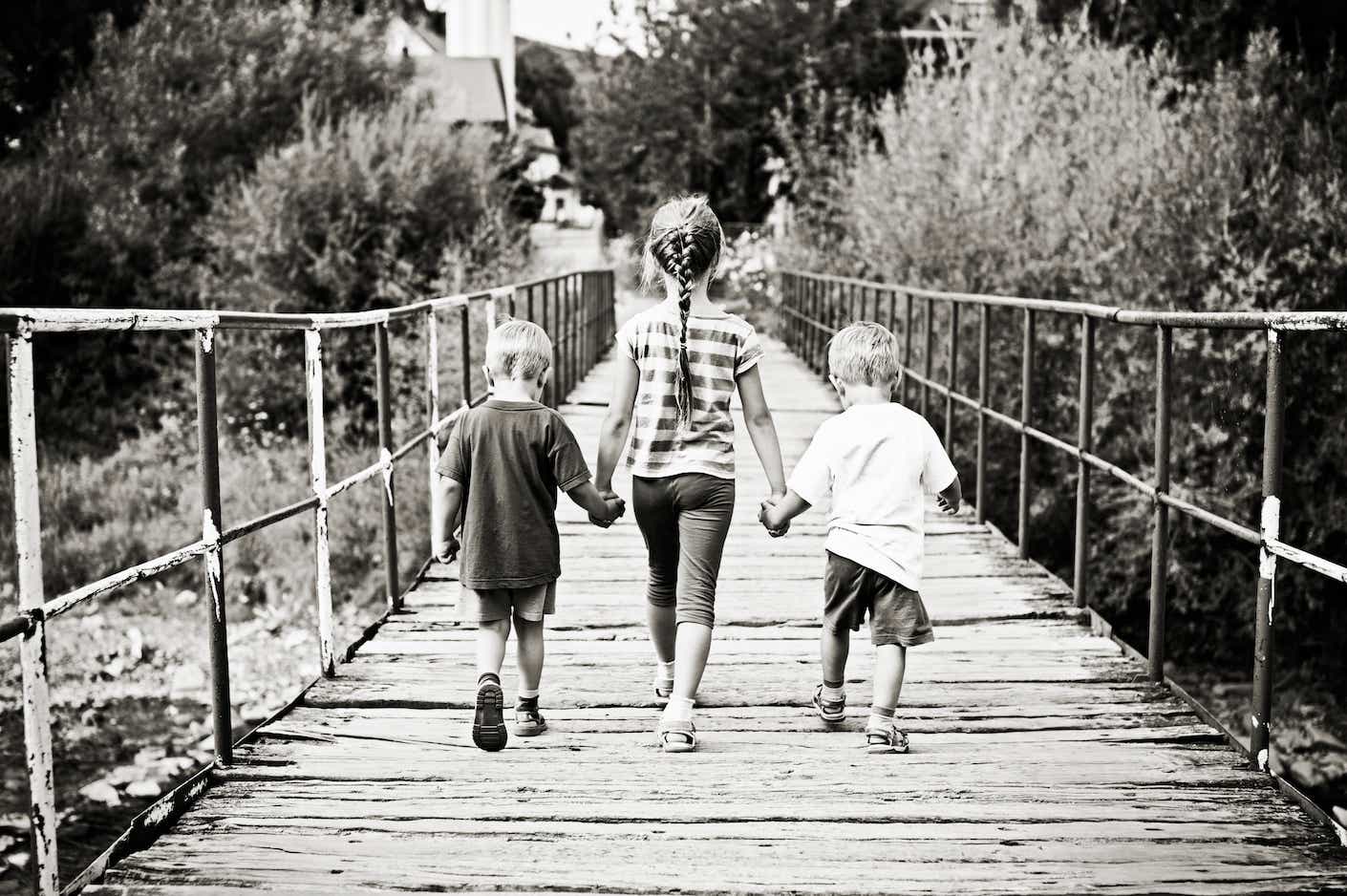 Sister and brothers crossing old bridge. 