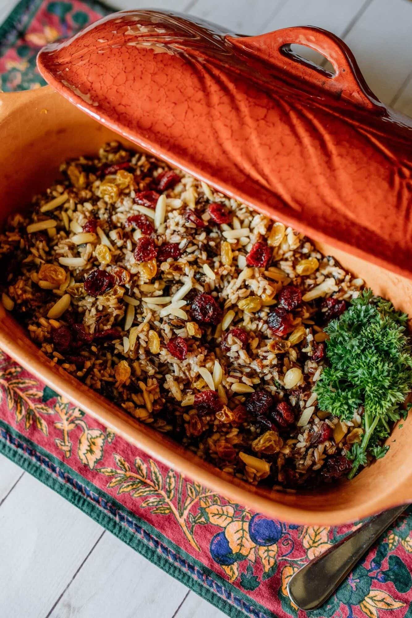 A roasting pan is full of a cranberry wild rice medley garnished with parsley.