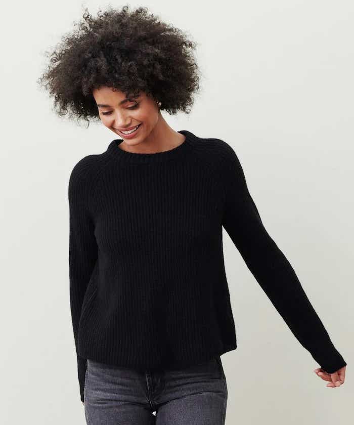 A woman wears a black, cashmere, fisherman sweater.