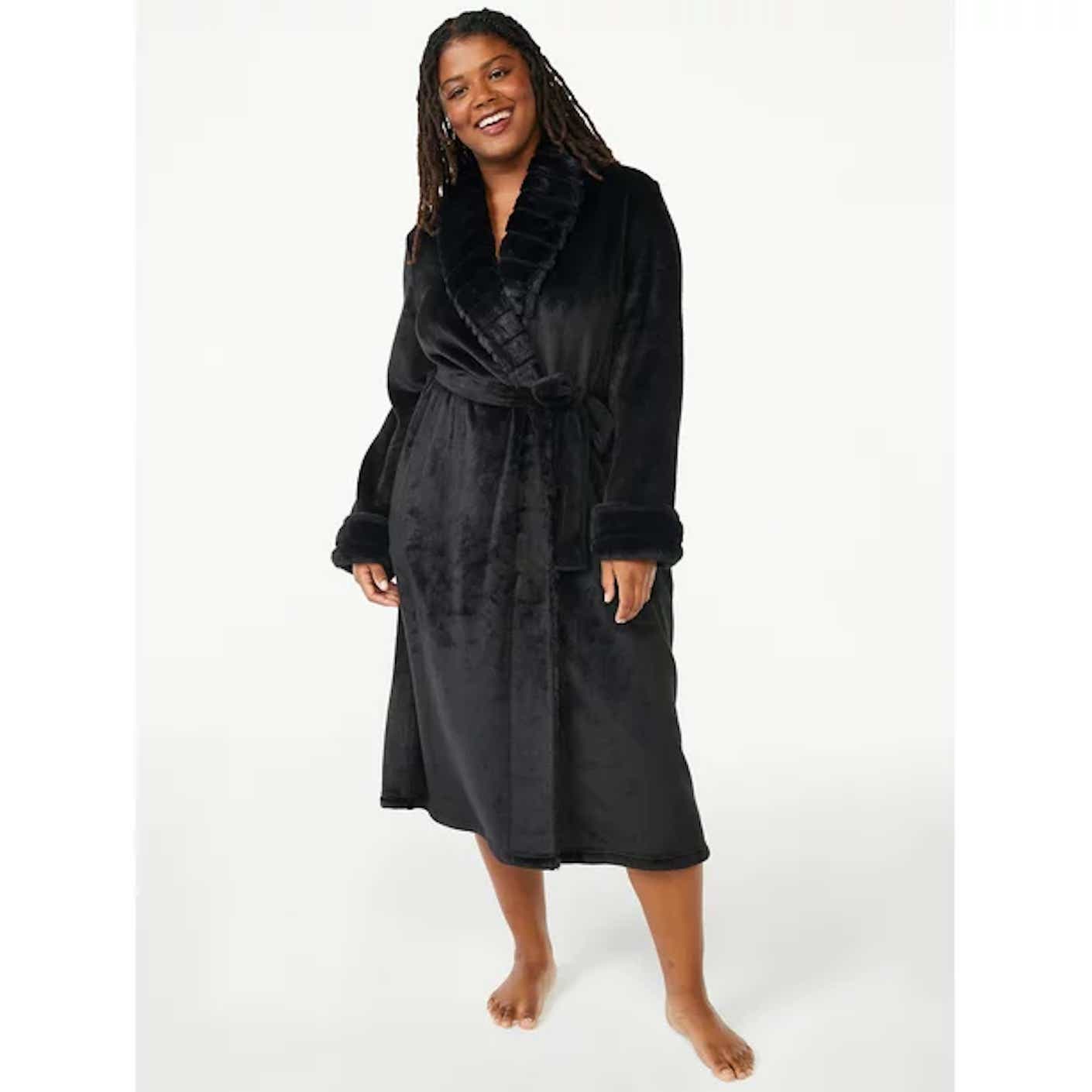 A woman smiles as she wears a black, plush robe that falls just below her knees.