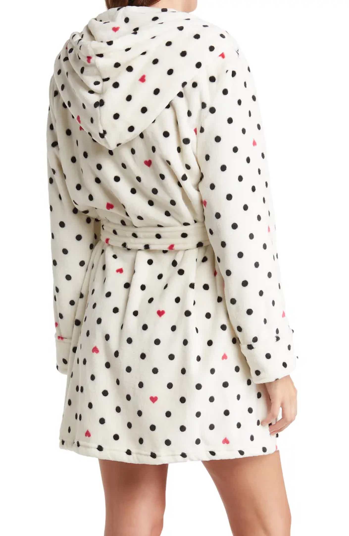A woman wears a plush, hooded, cream colored robe printed with black polta dots and small red hearts that hits at mid-thigh.