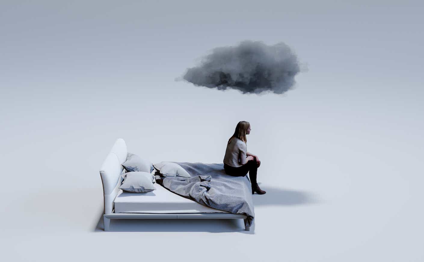 A woman sits in a gloomy bed while a cloud rains onto her head.