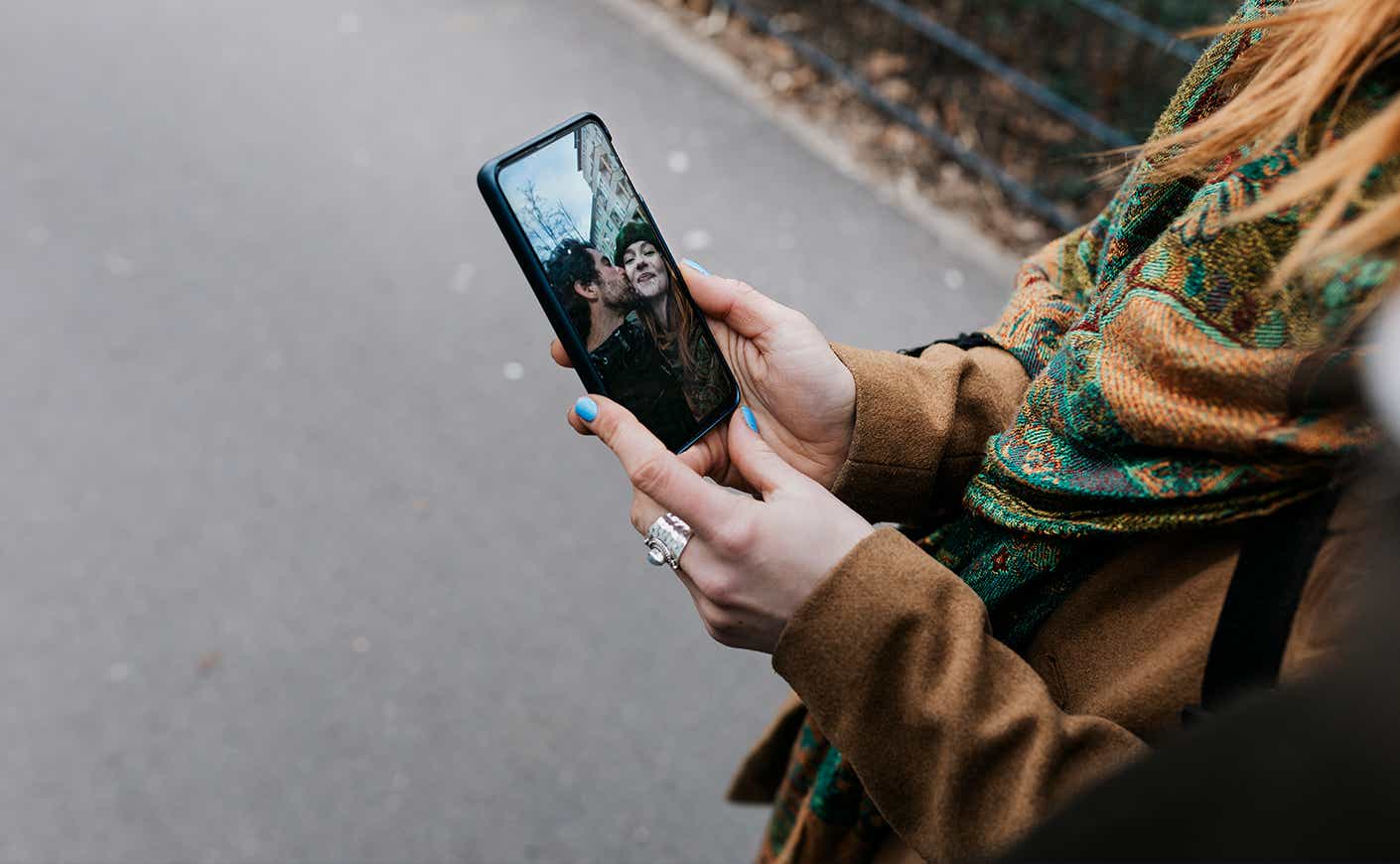 A woman showing her boyfriend a selfie she took of the two of them on her smartphone while out for a walk in the city together