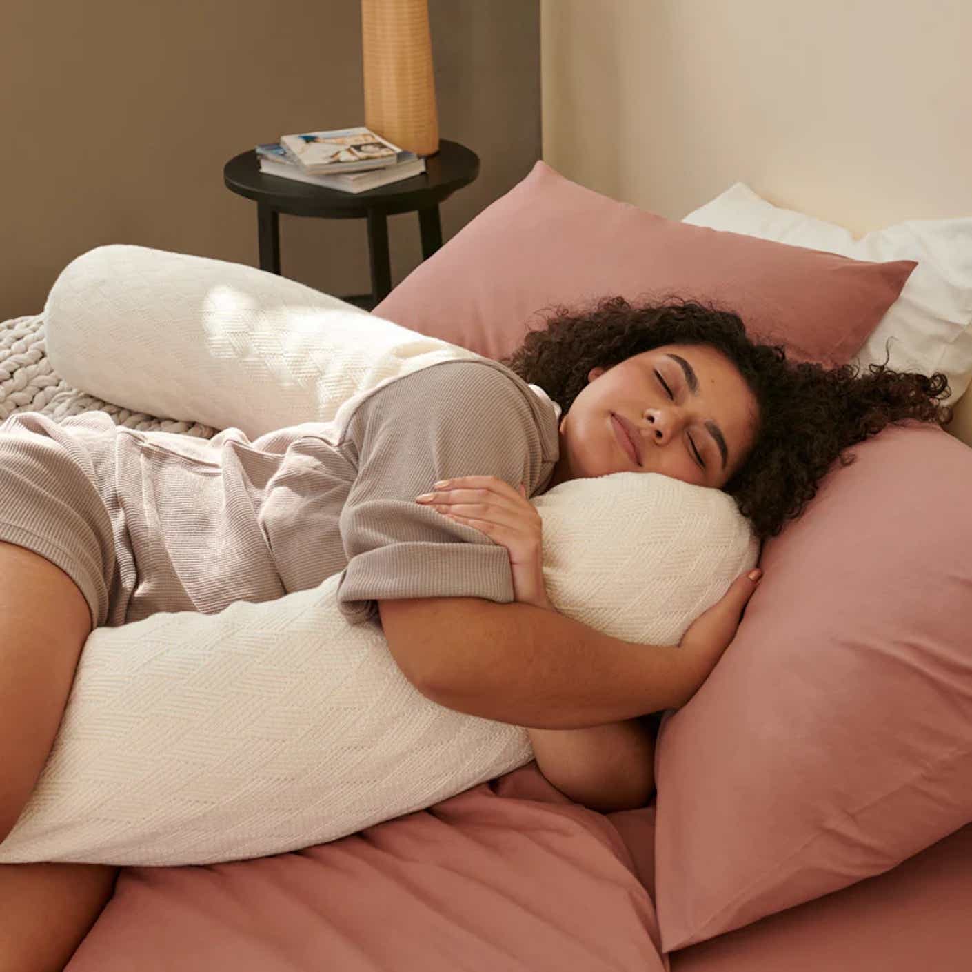 A woman blissfully hugs a body pillow in bed.