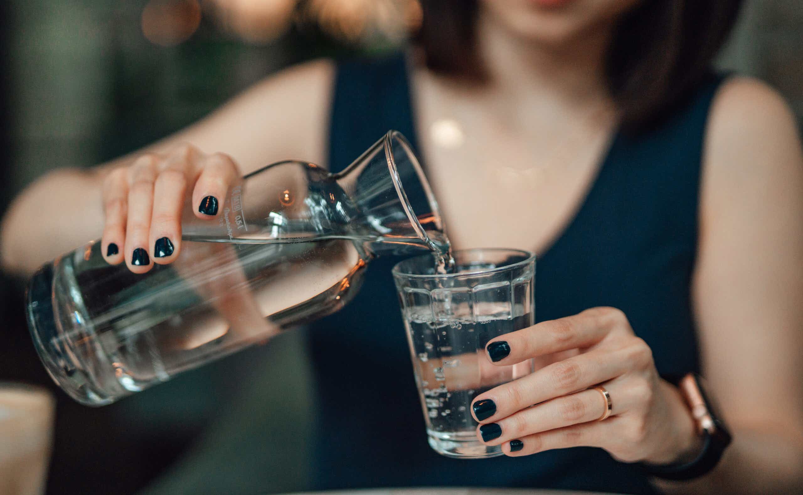 Cropped Shot Of Young Woman Pouring Water To A Drinking Glass At Cafe