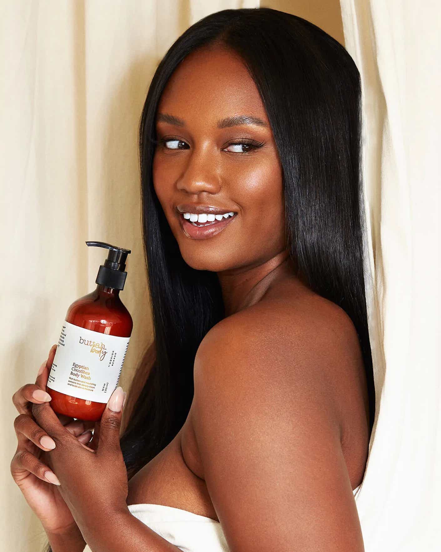 A woman smiles while holding a bottle of body wash.