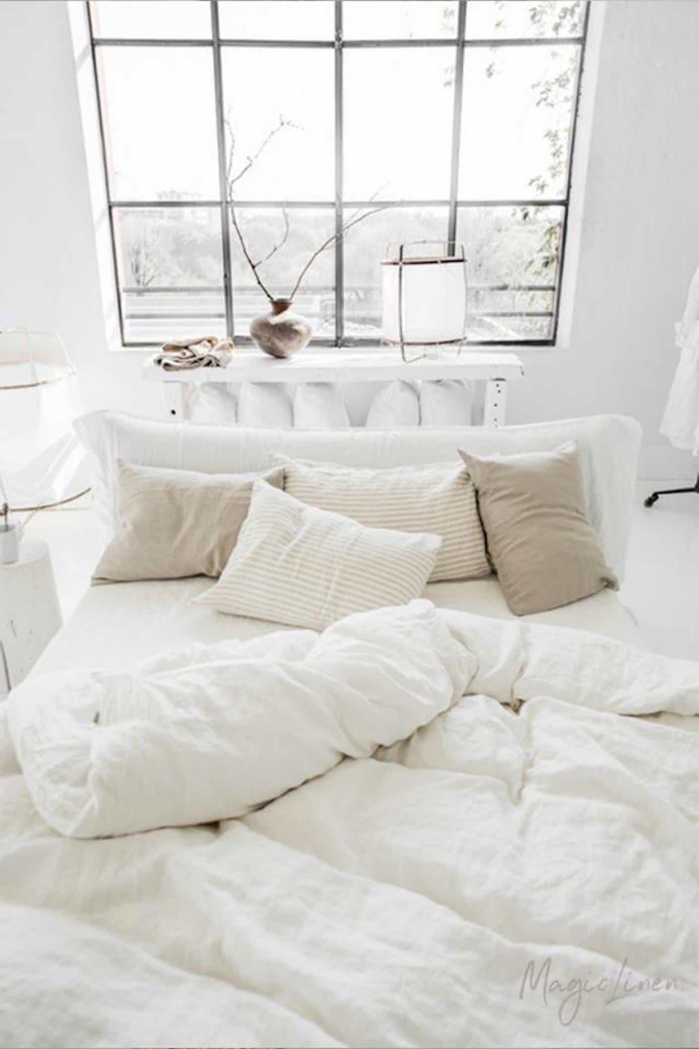 A white bed is covered in rumpled yet plush white sheets and duvet.