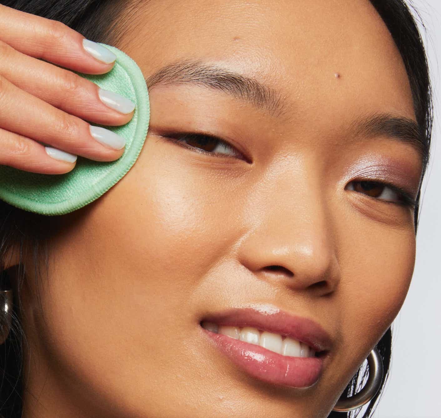 A woman wipes a disposable wipe onto her cheek.