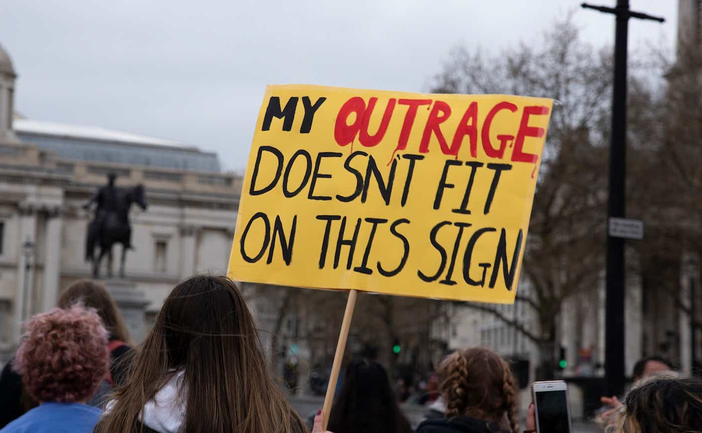 protestor holding a sign that says "my outrage doesnt fit on this sign"