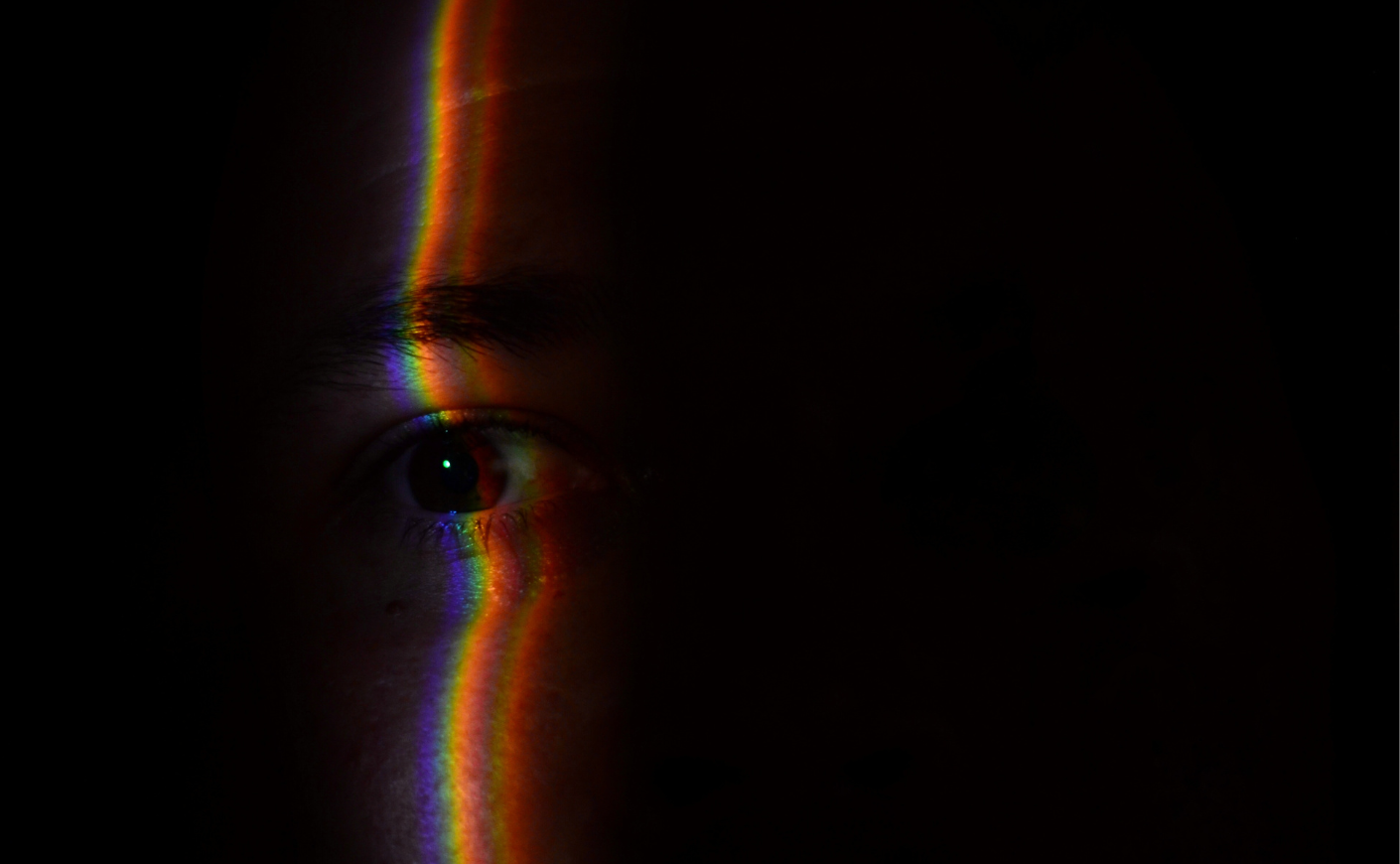 a face in the darkness with a rainbow stripe illuminating them