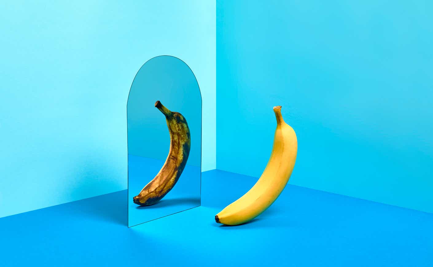 a yellow banana and its overripe reflection in a mirror