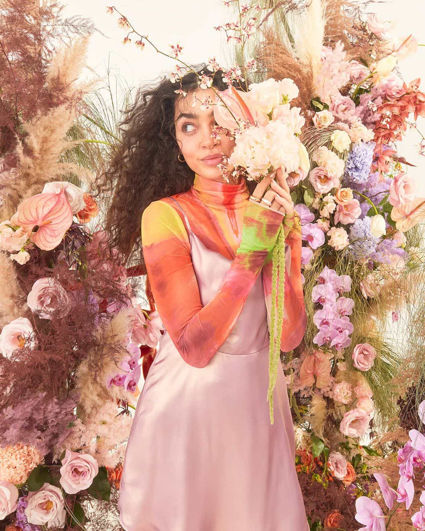 A woman wears silk and poses around flowers