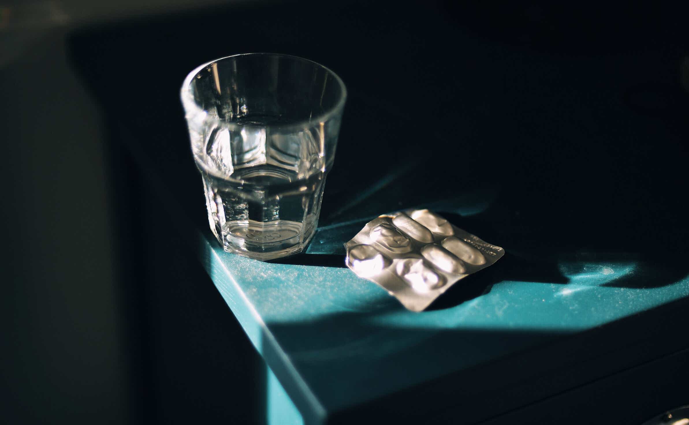 Glass of water and medication pills blister pack on bedside table