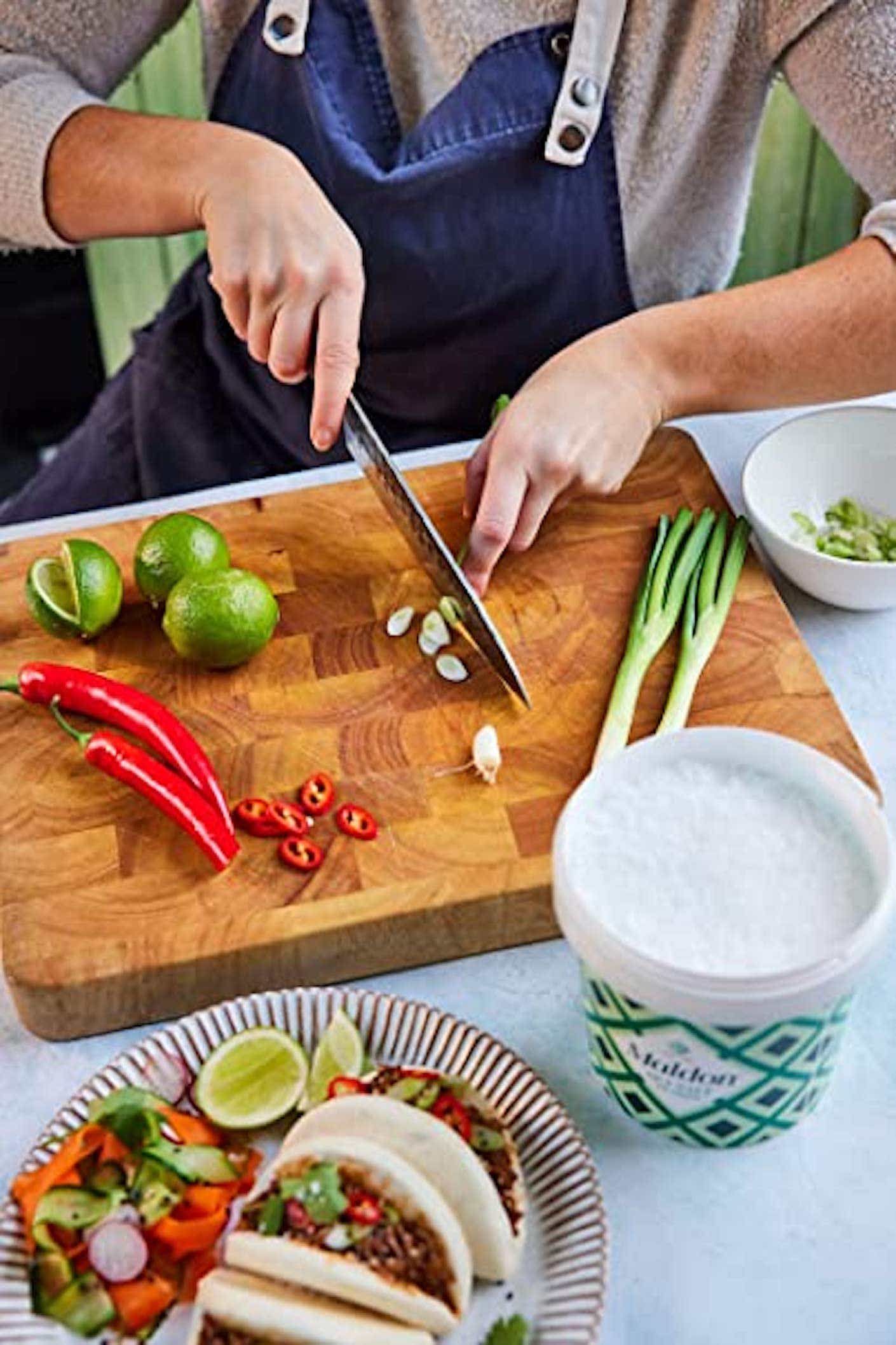 A person cuts vegetables next to a tub of salt